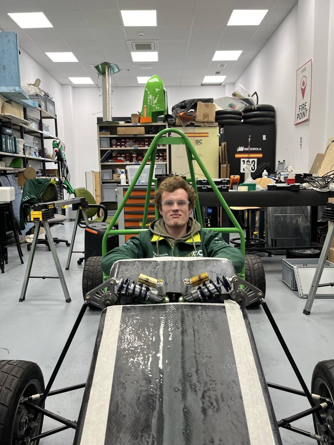 Miguel sitting inside a bare racing car frame in the workshop